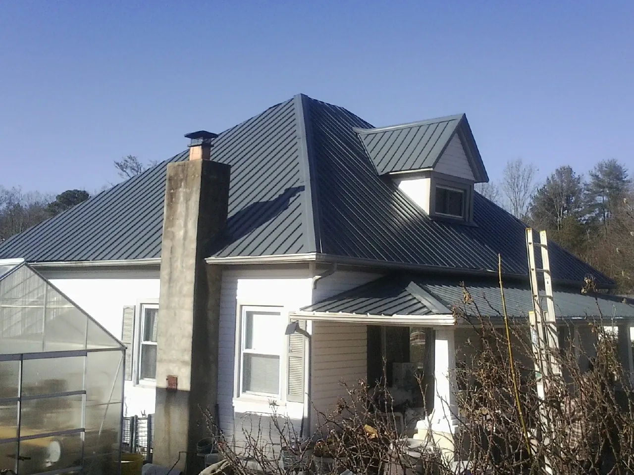Dark blue standing seam metal roof on a white farmhouse with dormer — Slate & Tile Roof Repair by Roofing Brothers in Kenansville