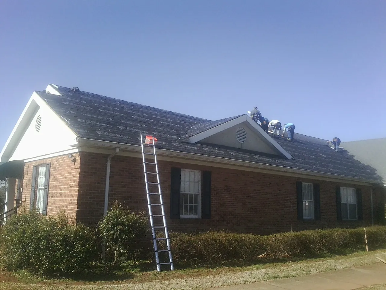 Crew tearing shingles off a brick ranch roof with a ladder set — Metal Roof Repair work by our crew in Kenansville