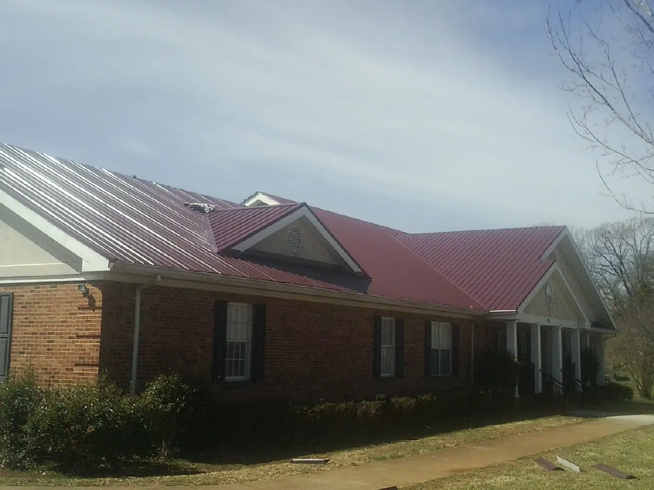Red metal roof with gabled entries on a long brick building, from a Hail Damage Roof Repair job in Kenansville