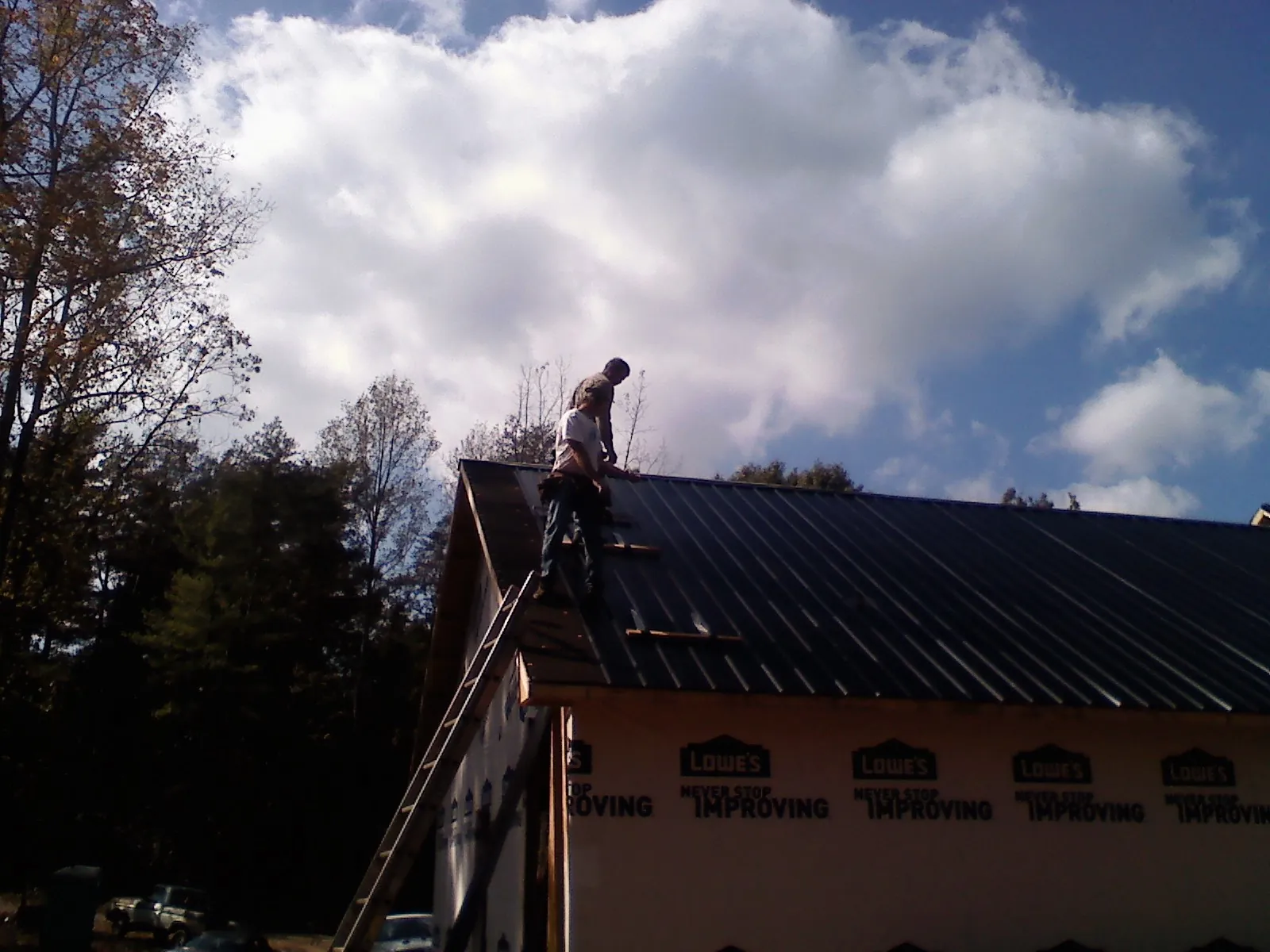 Roofer fastening dark metal panels high against a cloudy sky, from a Roof Inspection job in Kenansville