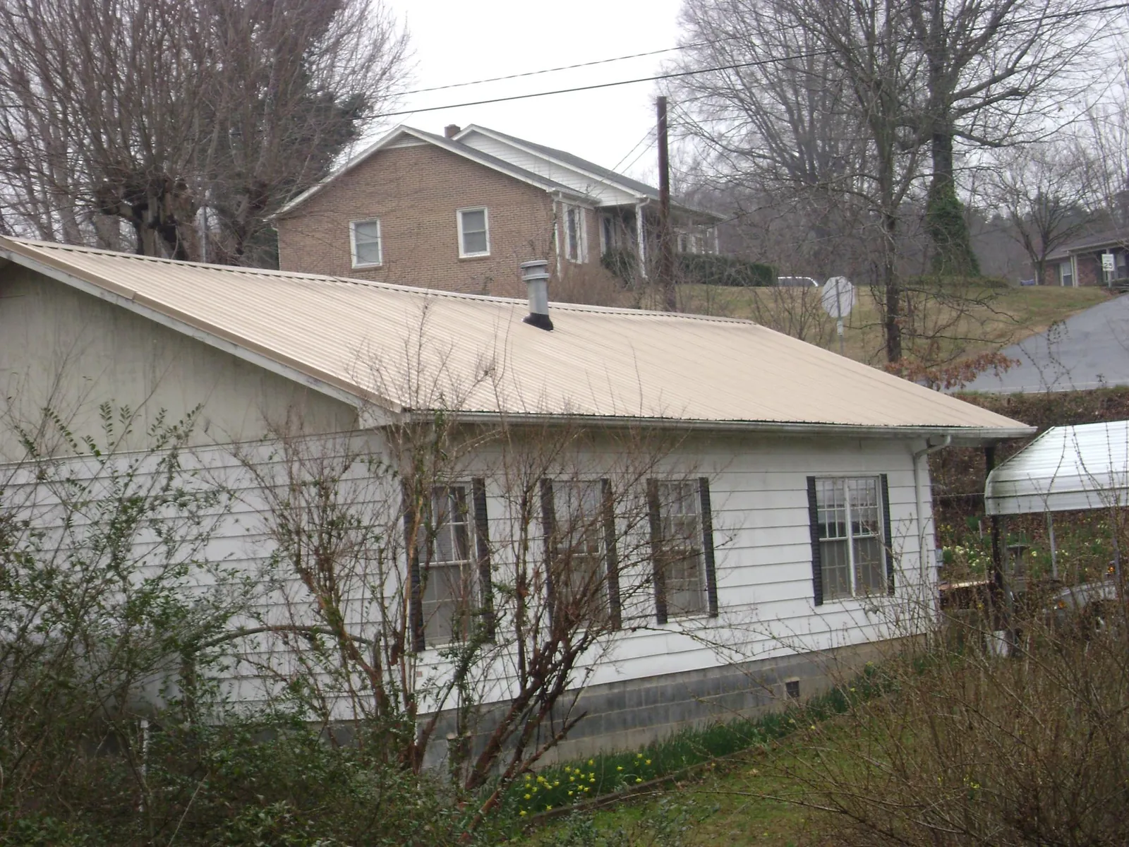 Tan metal roof on a white sided house set into a hillside — Commercial Roofing by Roofing Brothers in Kenansville